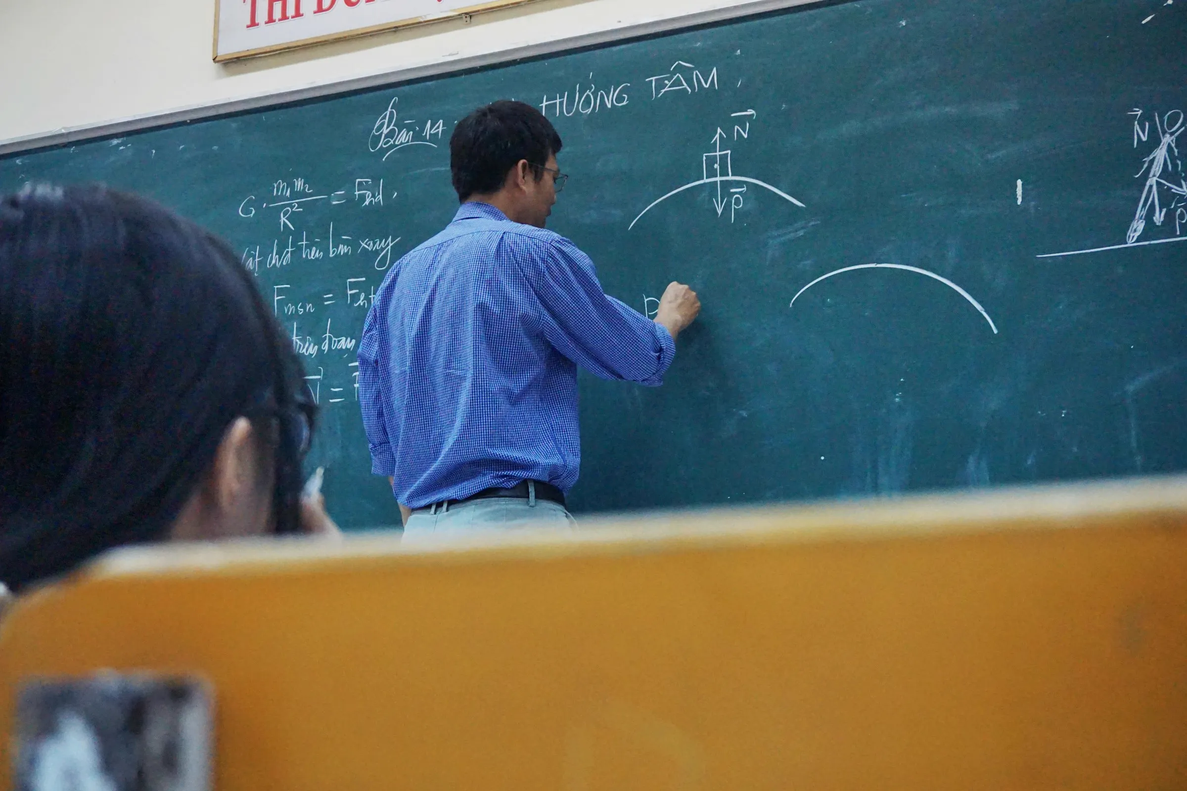 Un profesor escribe en la pizarra mientras la clase sigue la explicación