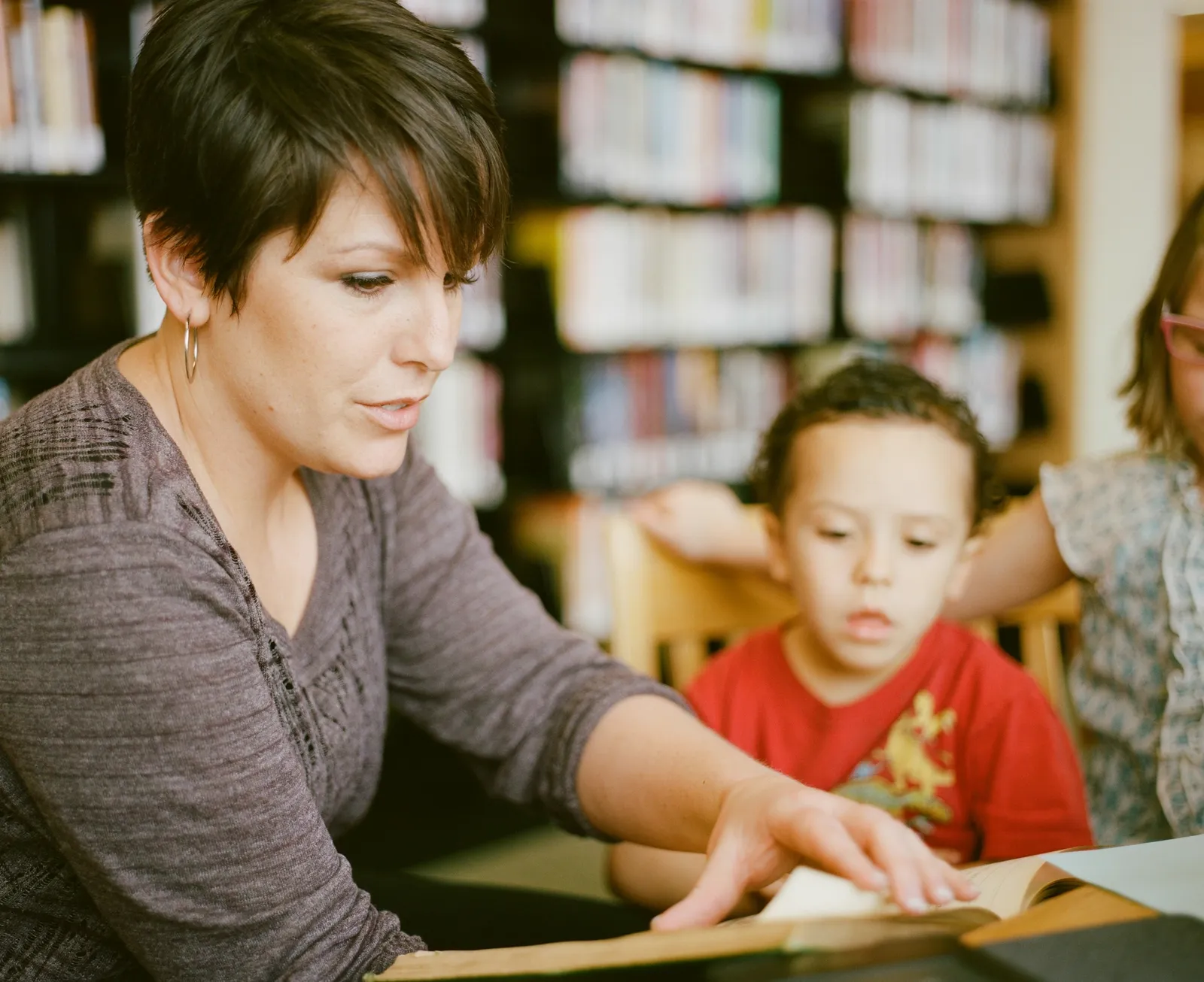 Una adulta acompaña a un niño en la lectura, rodeados de libros